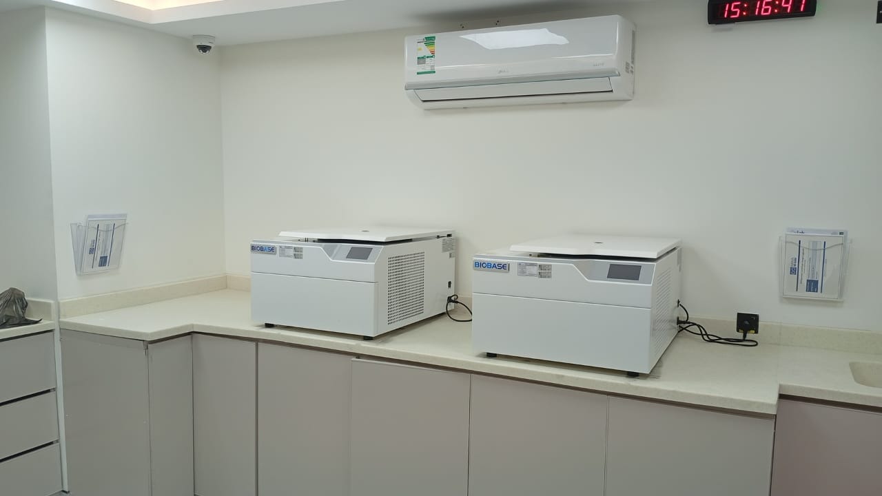 Two BIOBASE benchtop refrigerated centrifuges side by side on the sample preparation counter at NAMA Bio-Center, under a wall-mounted digital clock.